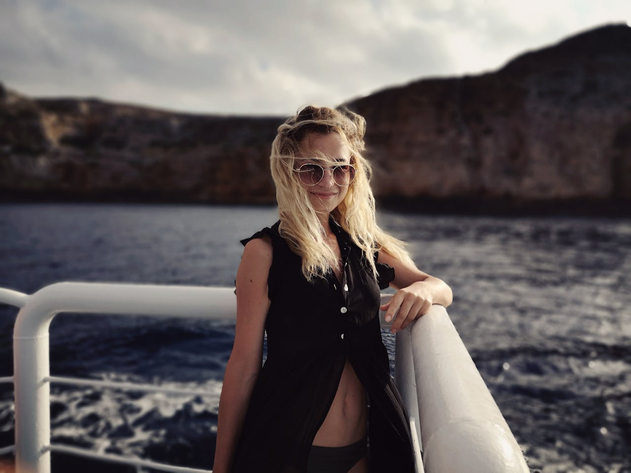 A young woman in sunglasses posing on a yacht with a scenic ocean view.