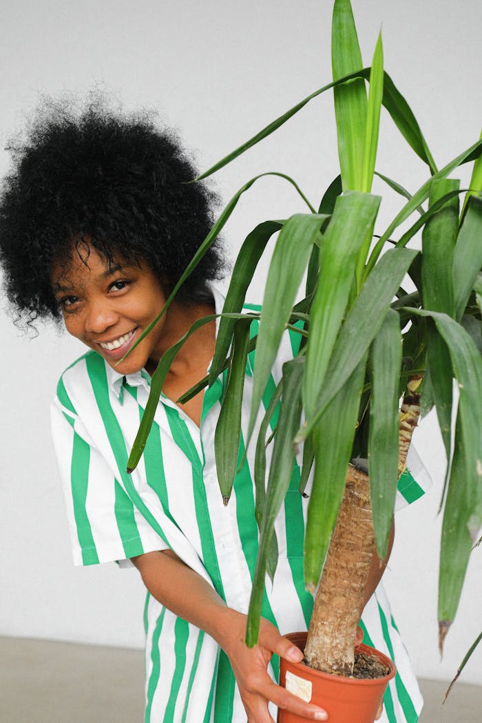 our-story-01 Cheerful woman holding a potted plant, expressing happiness in a casual striped shirt.